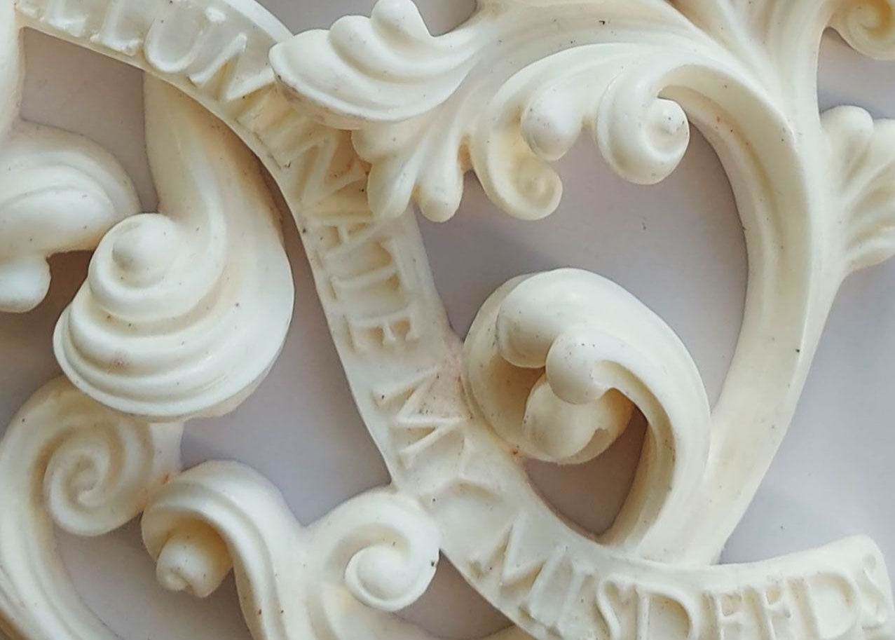 Detail of the ivory-coloured decorative artwork, Elephant of Light, showing stylised leaves, lettering and scrolls.