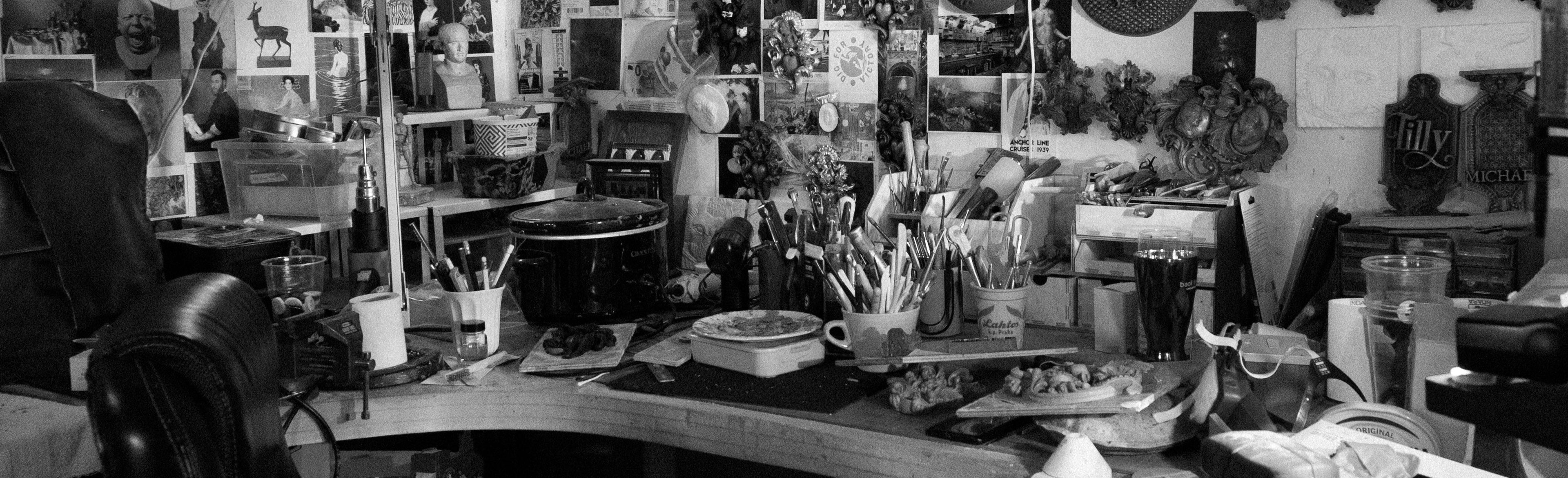 Black and white photograph of the artists work table and tools, and wall of postcards.